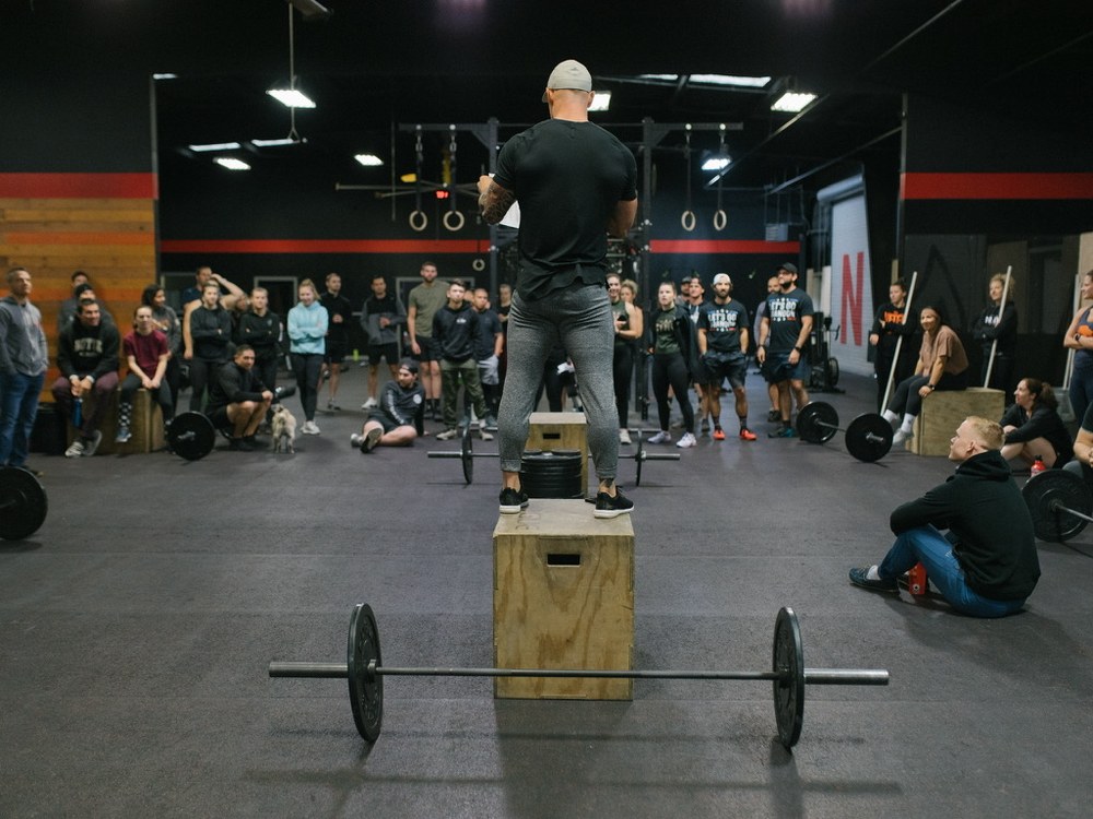 A packed group functional fitness class cheering on an athlete during a community box jump workout